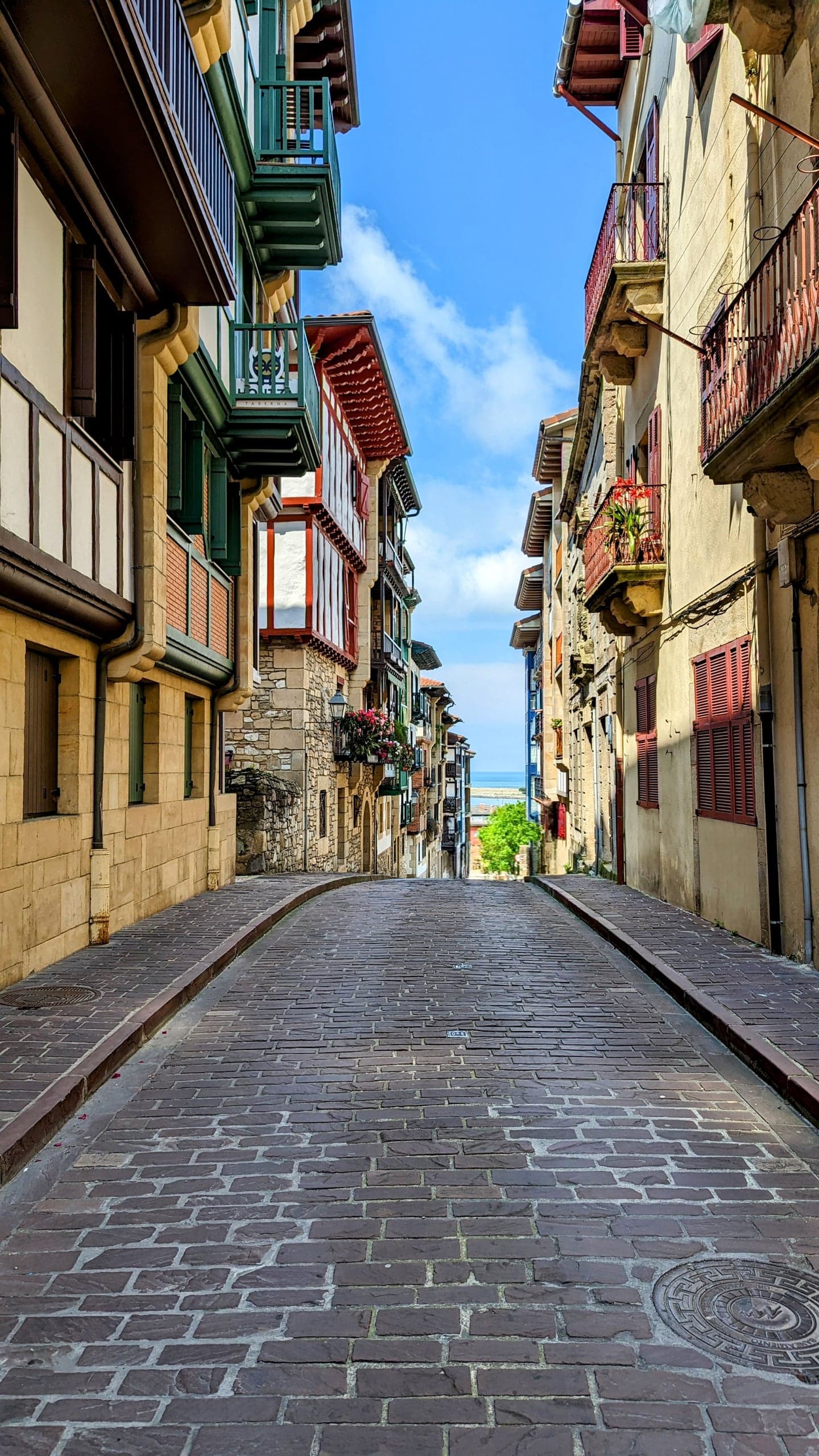A steep cobbled Hondarribia lane framed by colorful Basque balconies and a glimpse of sea