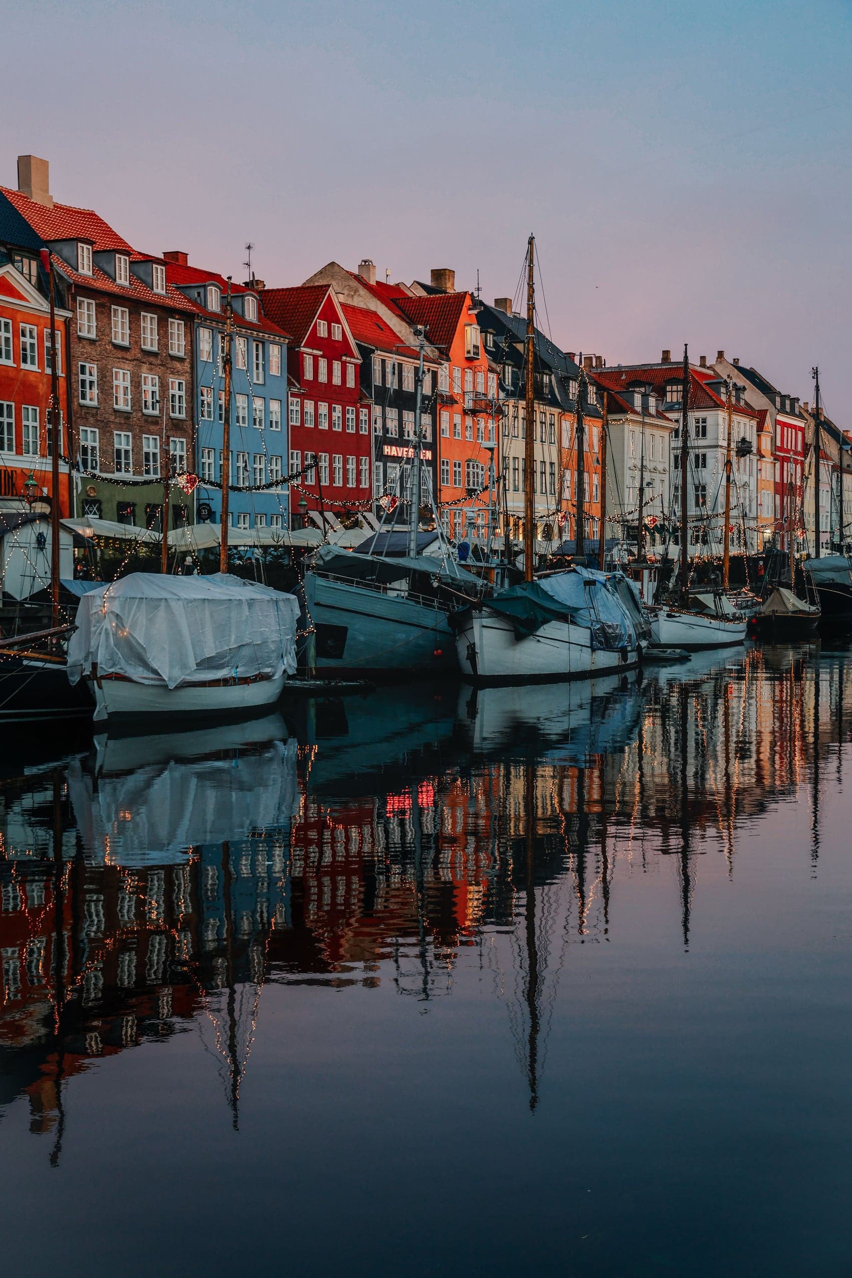 Nyhavn's red, blue, and ochre townhouses and old boats reflected in the canal at blue hour