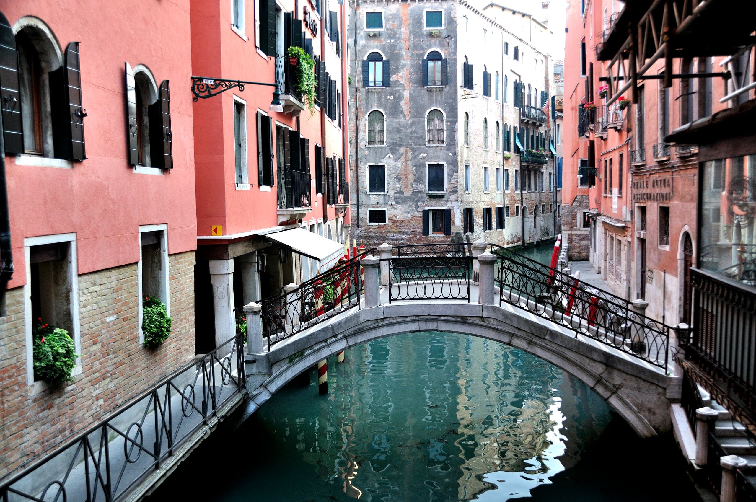 Quiet Venetian canal framed by red façades and an arched footbridge